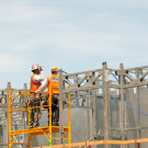 Two construction workers looking at the top of building frame